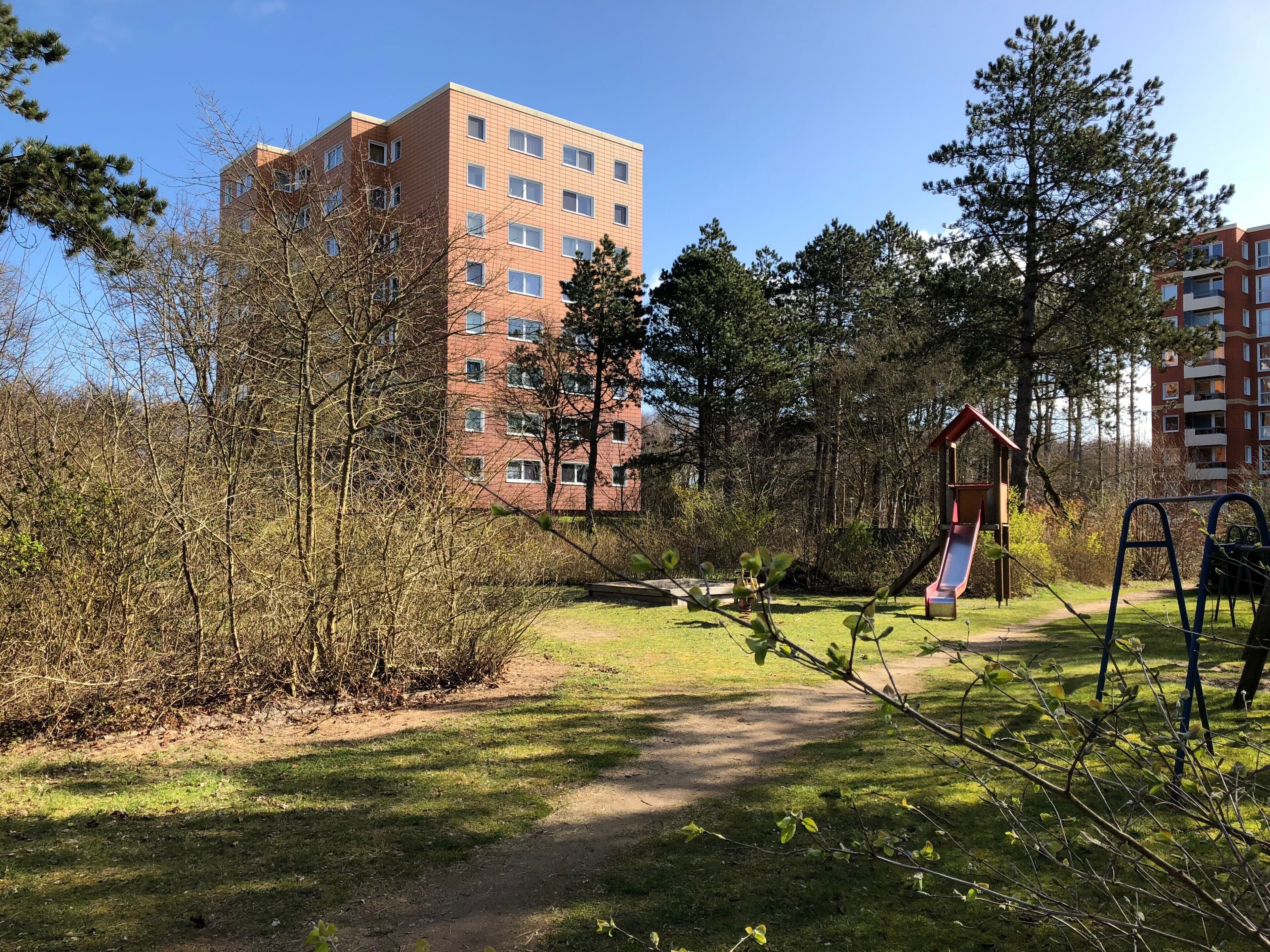 Un parc avec des jeux pour enfants, un sentier et un grand bâtiment en arrière-plan.