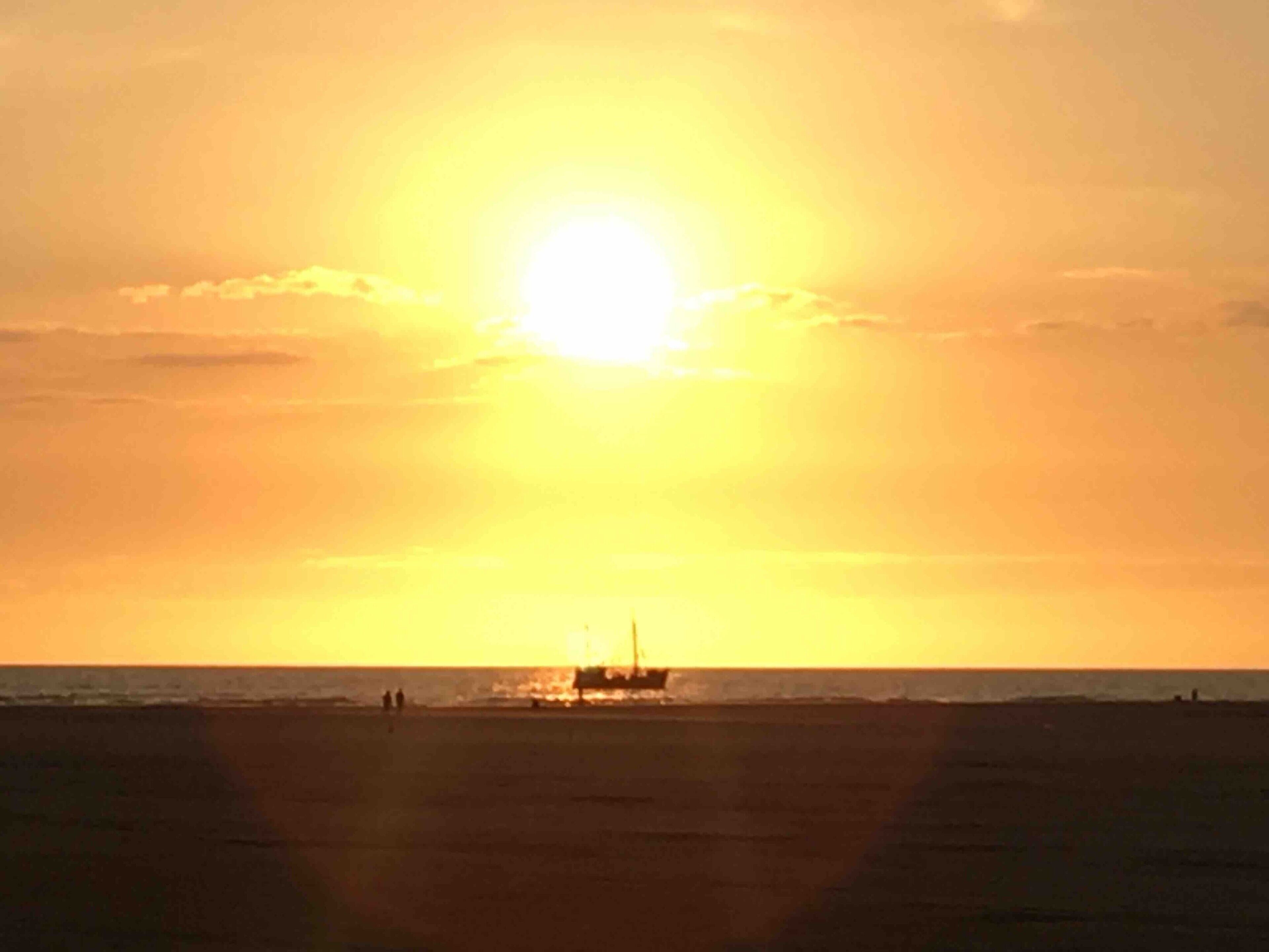 Een zonsondergang boven een strand, met een gebouw in de verte.