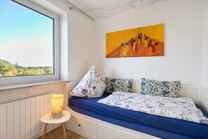 A bedroom with a bed, a lamp, a painting, and a view through a window.