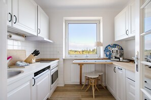 A modern kitchen with white cabinetry, a wooden countertop, a window with a view, and a small dining area.