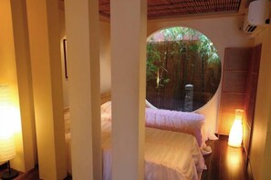 Ein Zimmer mit rundem Fenster, einem Bett, einer Nachttischlampe und einer Wand-Klimaanlage.