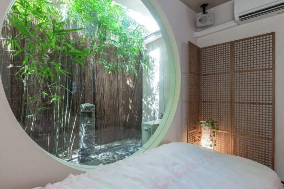 Une fenêtre circulaire donnant sur un jardin de bambous, un lit avec une literie blanche et un paravent japonais traditionnel.