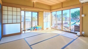 Una habitación con suelo de tatami, puertas correderas, un área de juegos visible a través del vidrio e iluminación empotrada en el techo.