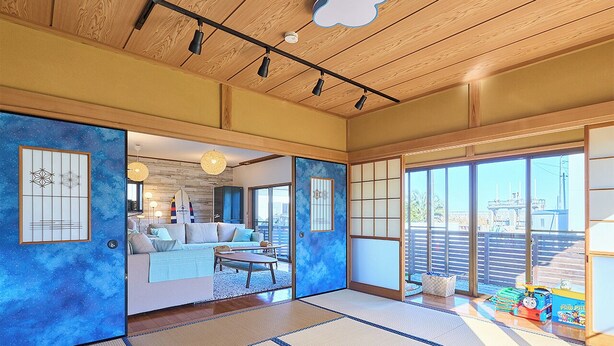 Una habitación tradicional japonesa con suelo de tatami, una puerta corredera que da a una sala de estar y grandes ventanales con vistas al exterior.
