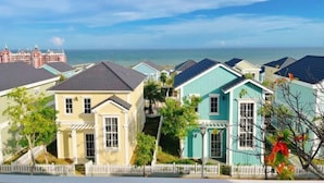 A coastal residential area with colorful houses, a white picket fence, and a view of the ocean. - Novaworld Phan Thiet - Alala Stay (Phan Thiet)