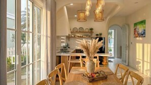 A dining area with a wooden table, chairs, and a vase of pampas grass. - Novaworld Phan Thiet - Alala Stay (Phan Thiet)