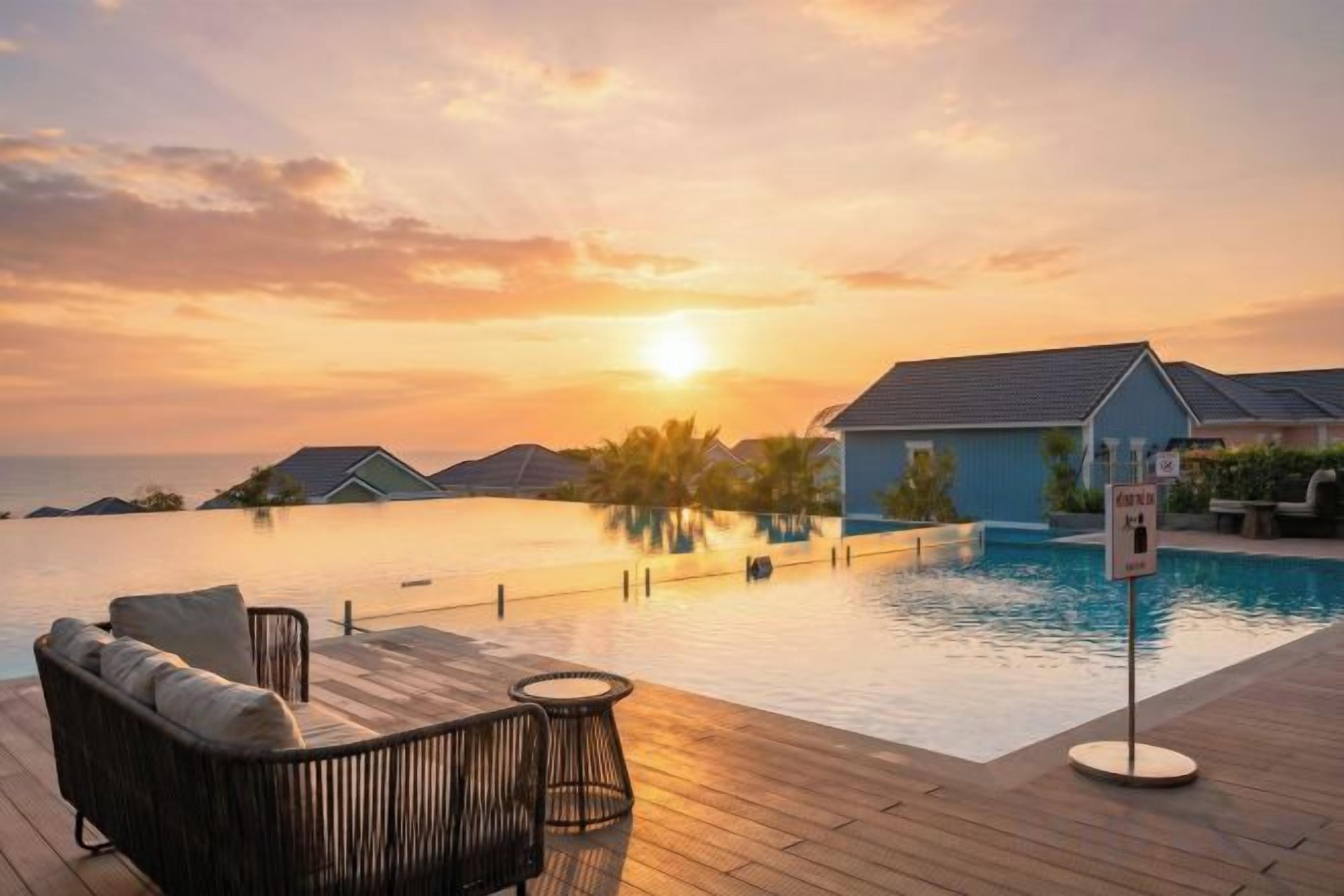 Una piscina infinita con cubierta de madera, sillas de descanso y bungalows sobre el agua.