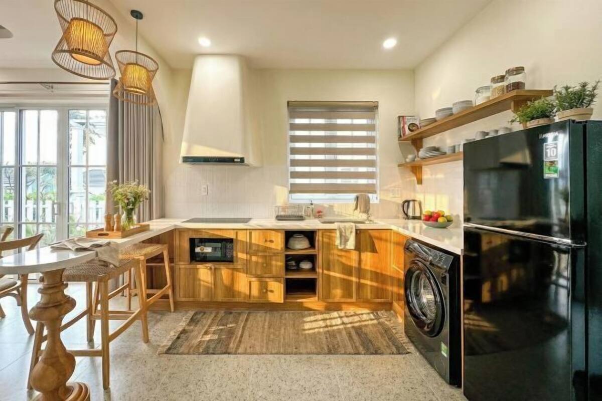 Une cuisine moderne avec des meubles en bois, un réfrigérateur noir, un lave-linge et un coin repas comprenant une table et des chaises.