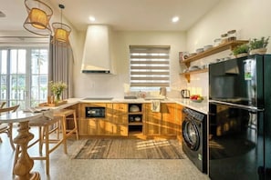 A modern kitchen with a built-in washing machine, a black refrigerator, and a dining area with wooden chairs.