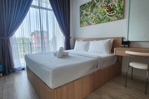 Una camera d'albergo con un letto, una scrivania e una sedia. Si vede una finestra con tende e un quadro appeso al muro.
