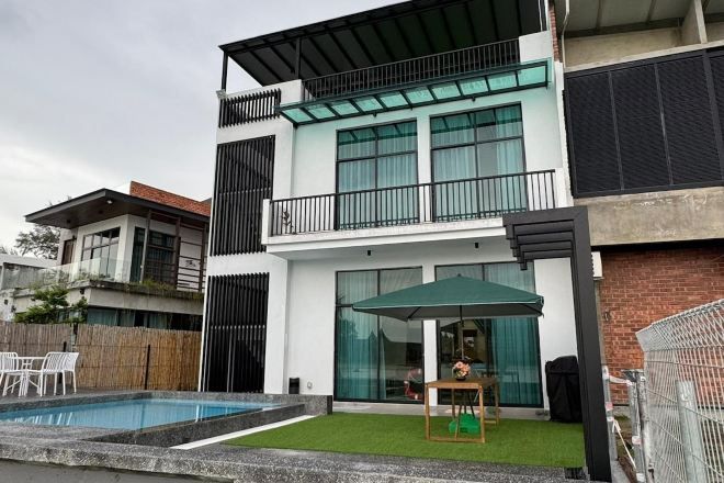 A modern two-story house with a swimming pool, a balcony, and a patio area with outdoor furniture.
