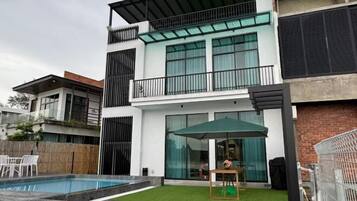 A modern two-story house with a swimming pool, a balcony, and a patio area with outdoor furniture.
