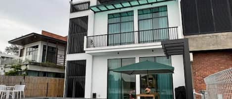A modern two-story house with a swimming pool, a balcony, and a patio area with outdoor furniture.