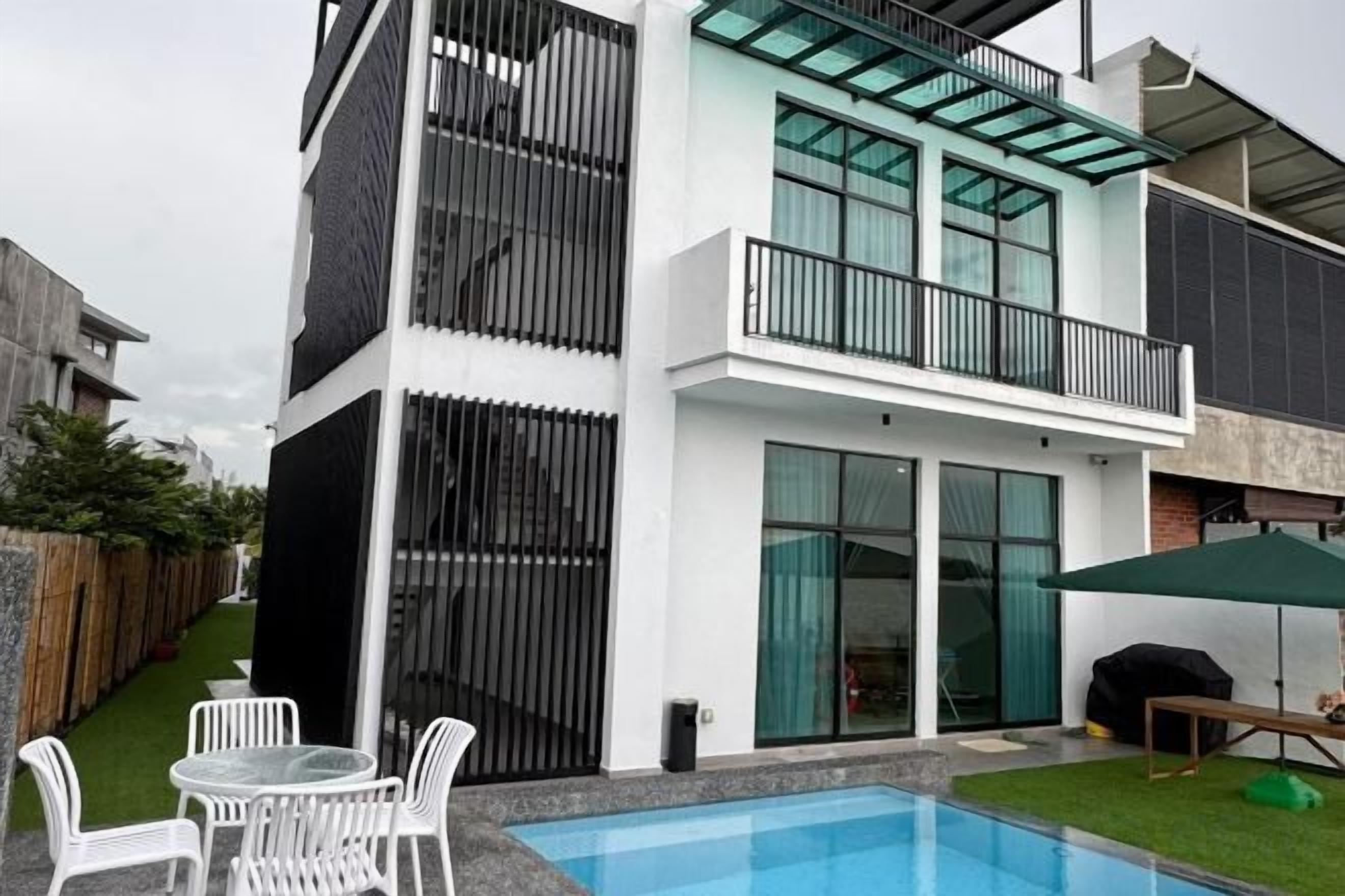 A modern two-story building with a glass balcony, a swimming pool, and outdoor seating.