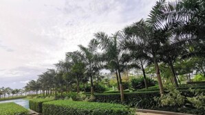 A landscaped garden with palm trees, a pool, and neatly trimmed hedges. - Private Lift 5star Home Seaview Permas / Senibong Cove / Mid Valley Johor (Masai)