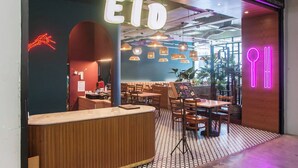 Ein modernes Restaurantambiente mit einer Neonreklame 'EID', Holztischen und hängenden Pendelleuchten.