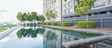 A modern residential building with a swimming pool, surrounded by greenery and a clear sky.