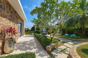 A modern house with a stone exterior, a paved pathway, and lush greenery including a palm tree. - Turquoise Villa 2 GYM and KIDS ROOM (Koh Samui)