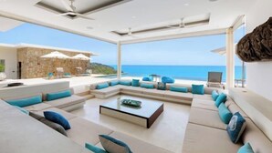 A modern living room with a large window overlooking the sea, a stone wall, and a seating area with cushions. - Turquoise Villa 2 GYM and KIDS ROOM (Koh Samui)