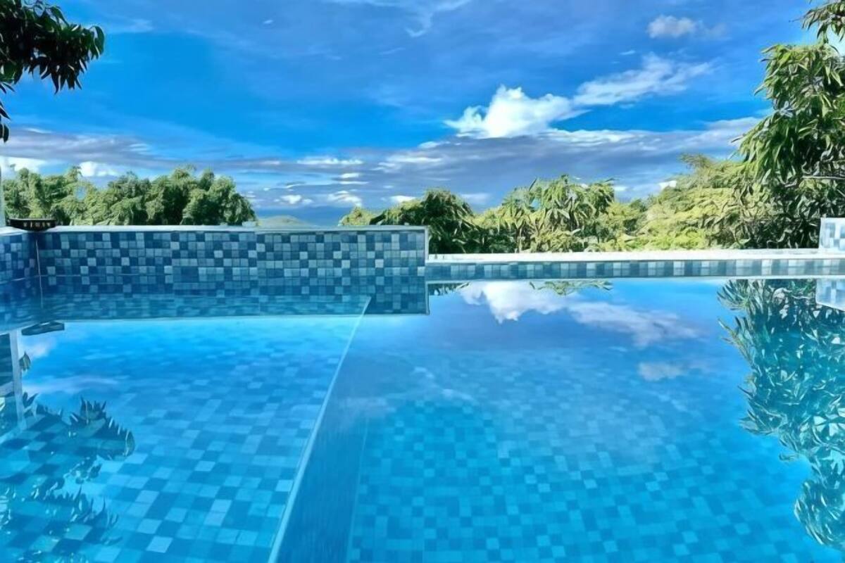 Piscina infinita azul cristalina con borde de azulejos, rodeada de exuberante vegetación y un cielo despejado.
