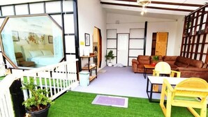 Een kamer met een vloer van groen kunstgras, een bruine bank, een houten tafel en een witte stoel. Links staat een witte schutting met een plant in een pot.