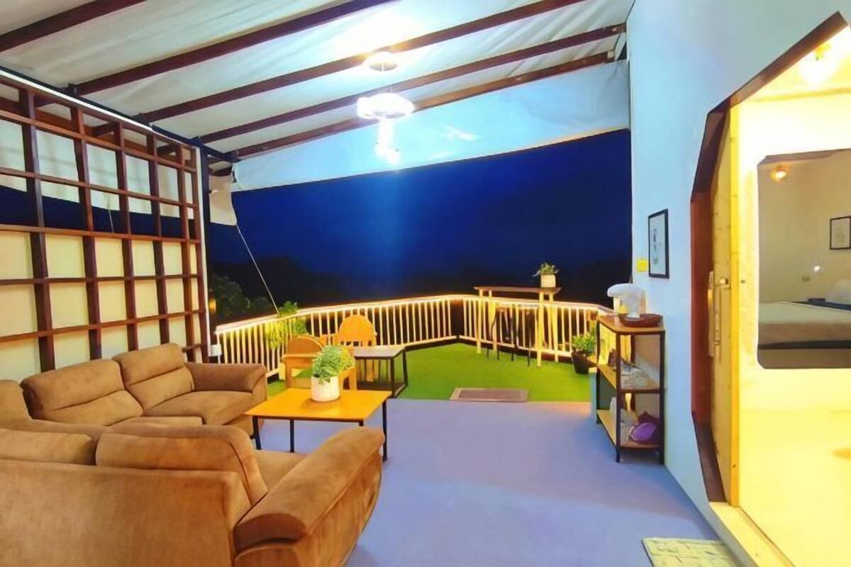 Una habitación con un sofá, una mesita con una planta, una lámpara y vistas a un balcón con barandilla.