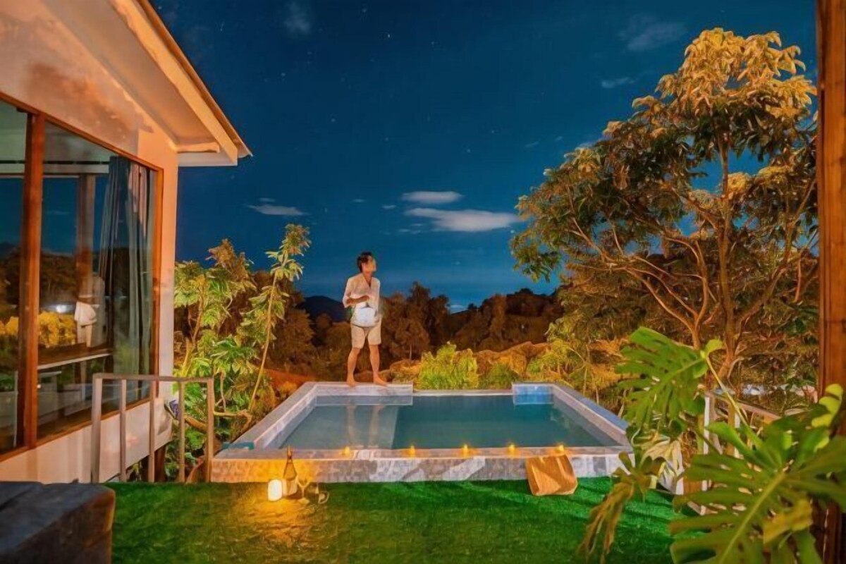A person standing by a swimming pool with a view of the night sky and surrounding greenery.