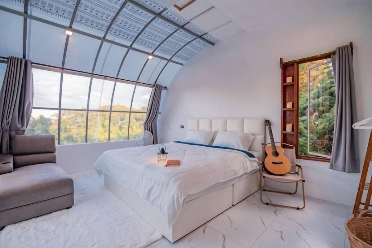 Un dormitorio con un tragaluz grande, una cama, una guitarra, una silla y vistas al exterior.