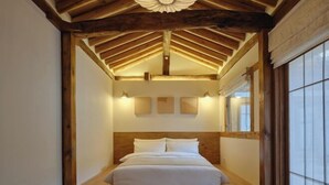 Ein Schlafzimmer mit Schrägwand, Holzbalken, einem Bett, Wandleuchten und einem Fenster.