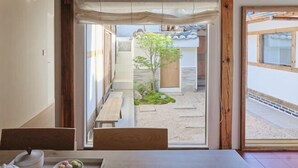 Ein traditioneller japanischer Raum mit Tatami-Boden, einem niedrigen Tisch mit Tee-Service und Blick auf einen Garten durch eine Schiebetür.