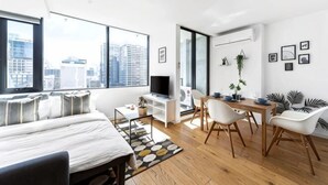 A modern bedroom with a bed, a desk, and a chair. There is a large window with a city view. - Spacious Southern Cross Stay, Cozy & Central Home (Melbourne)