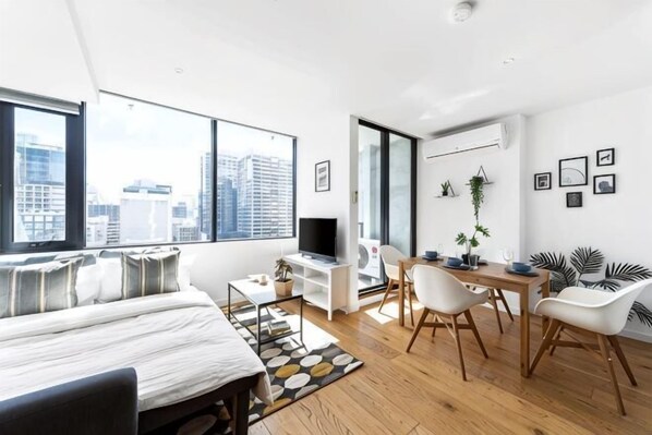 A modern bedroom with a bed, a desk, and a chair. There is a large window with a city view.