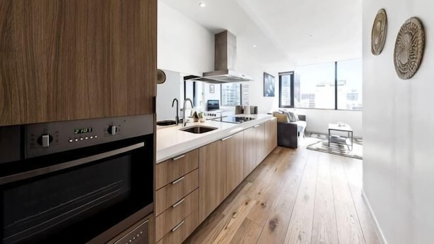 A modern kitchen with wooden cabinets, a built-in oven, and a large window overlooking the city. - Spacious Southern Cross Stay, Cozy & Central Home (Melbourne)