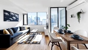 A modern living room with a sofa, dining table, chairs, and a city view through large windows. - Spacious Southern Cross Stay, Cozy & Central Home (Melbourne)
