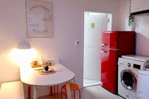 Uma cozinha compacta com uma mesa branca, geladeira vermelha e máquina de lavar.