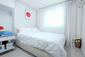 Una habitación de hotel con cama, mesita de noche, espejo y ventana con cortinas.