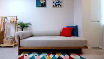 Quarto com sofá, tapete colorido, uma pequena planta e obras de arte nas paredes.