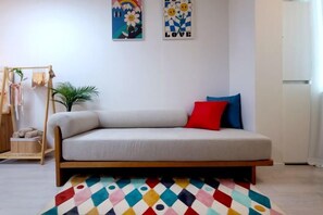 Quarto com sofá, tapete colorido, uma pequena planta e obras de arte nas paredes.