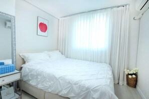 Quarto de hotel com cama, mesa de cabeceira, espelho, decoração de coração na parede e janela com cortinas.