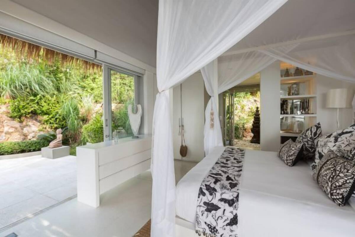 Une chambre à coucher avec un lit à baldaquin, une vitrine et une vue sur la verdure environnante.