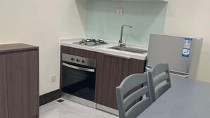 A compact kitchen with a gas stove, sink, oven, and a refrigerator. There is a dining table with chairs. - orkide apartment (Phnom Penh)