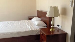 A neatly made bed with white linens, a wooden nightstand with a lamp, and a wall socket. - orkide apartment (Phnom Penh)