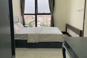 Un dormitorio con cama, ventana y vista a un paisaje urbano.