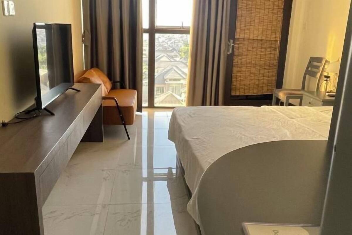 A hotel room with a bed, a desk, a chair, a TV, and a view of the outside.