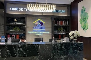 Un mostrador de recepción con una araña, un letrero de Orkide Development y una estantería con libros y plantas.