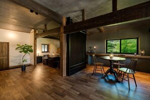 A spacious room with a wooden floor, a dining area with chairs, a table, and a large window with a view.