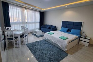 A modern bedroom with a bed, bedside tables, a desk, and chairs. - HRG Hurghada Aparthotel Aqua park A100 - By MAMO Property (Hurghada)