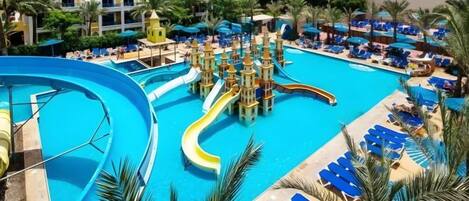 A large pool with multiple slides and water features, surrounded by lounge chairs and palm trees.