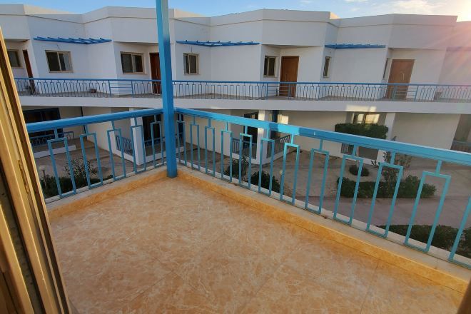 Un edificio de varios pisos con balcones, barandilla azul y cielo despejado.