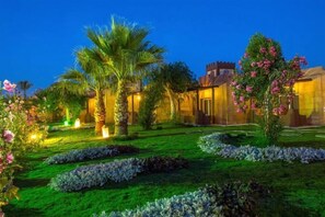 A well-maintained garden with palm trees and flowering plants, a building with a traditional architectural style, and a clear sky. - HRG Hurghada Aparthotel Aqua park A100 - By MAMO Property (Hurghada)